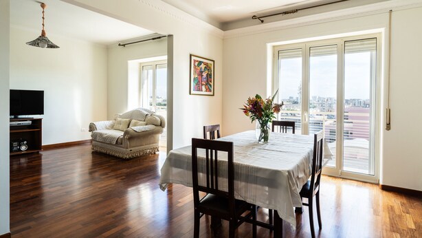 Un coin repas avec une table dressée pour deux personnes, un canapé et un téléviseur, dans une pièce dotée d’un plancher en bois et de grandes fenêtres.