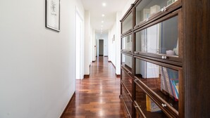 Un long couloir au sol en bois, aux murs blancs, et sur le côté droit, une grande armoire en bois dotée de portes en verre.