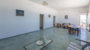A spacious living area with a glass coffee table, a sofa, a dining table with chairs, and a view of the outdoors.