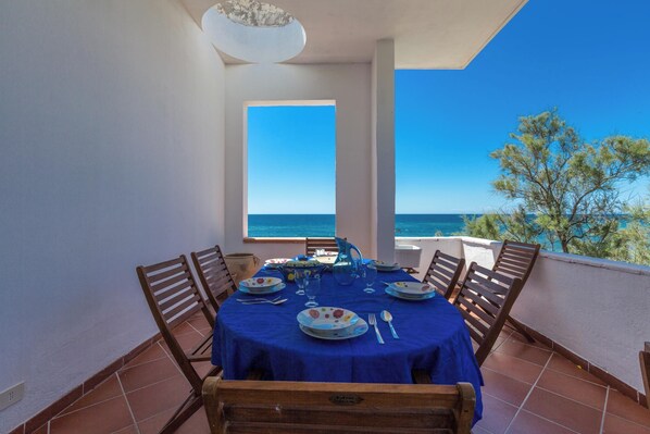 Une table à manger dressée pour quatre personnes sur un balcon offrant une vue dégagée sur la mer.