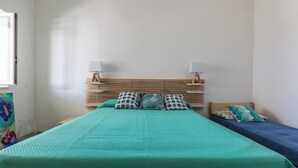 A room with a large bed, two bedside lamps, and a smaller bed.