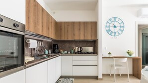 A modern kitchen with wooden cabinets, a built-in oven, a coffee maker, and a clock on the wall. - Mary House by BarbarHouse (Talsano)
