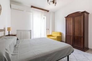 Un dormitorio con una cama, un sillón amarillo, un armario de madera, un radiador y una ventana con cortinas.