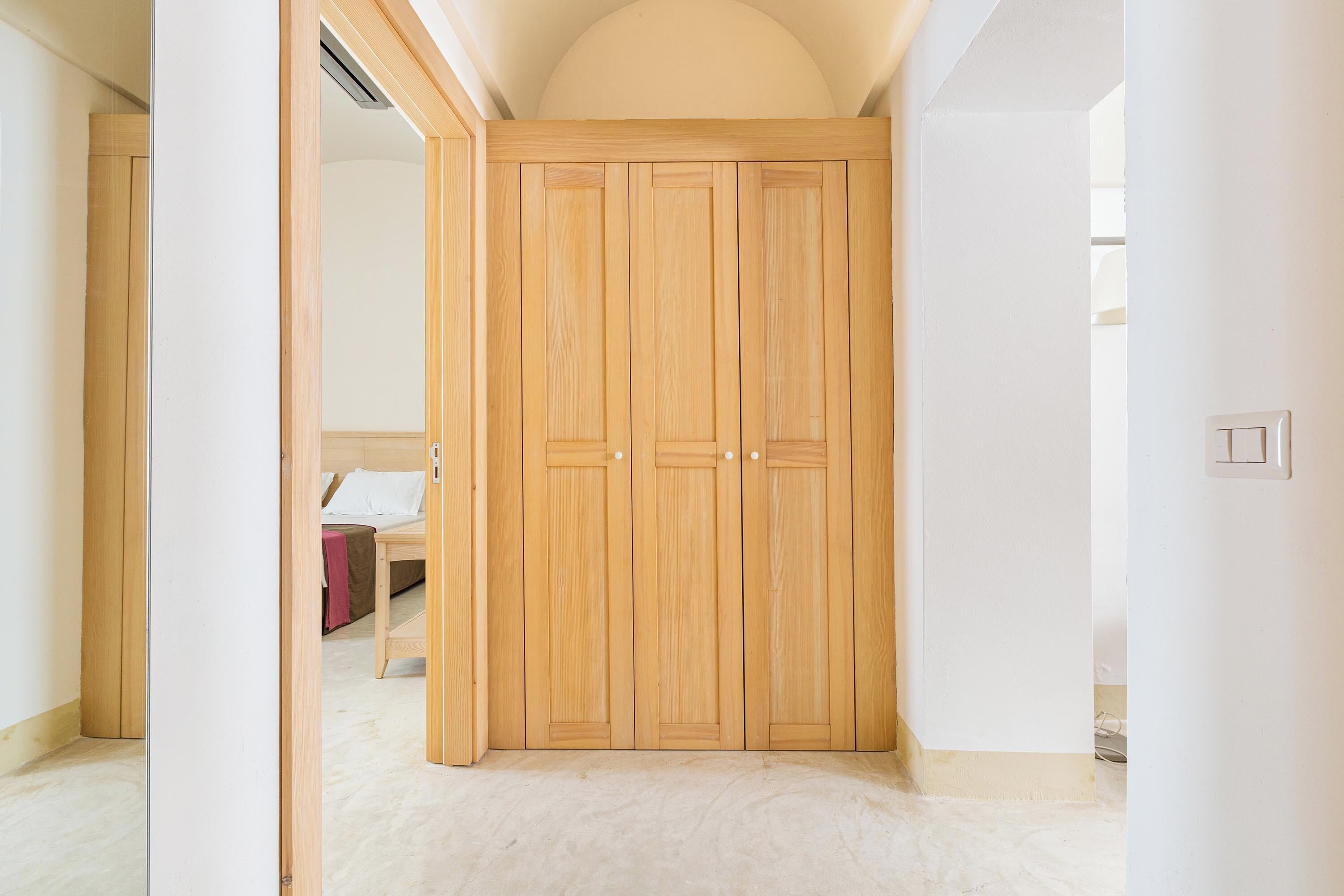 A room with a wooden wardrobe, a bed, and a bedside table.