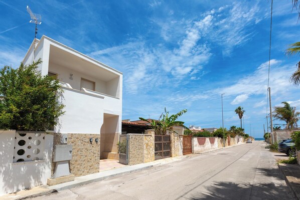 A modern white house with a stone wall, a metal gate, and a clear view of the street and ocean. - A due Passi dal Mare - PT by BarbarHouse (Spiaggia Bella)