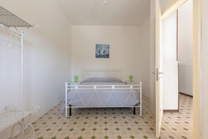 A bedroom with a bed, a small table, a chair, and a painting on the wall. - A due Passi dal Mare - PT by BarbarHouse (Spiaggia Bella)