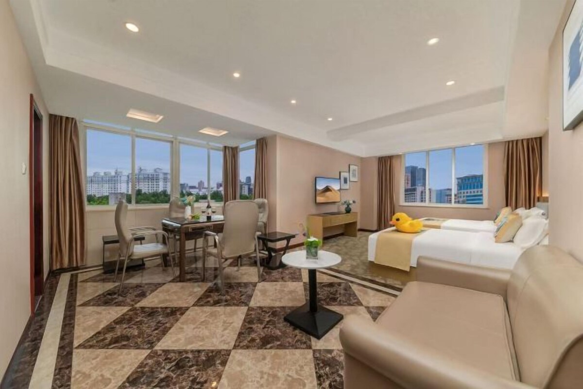 A hotel room with a city view, a dining area, a sofa, and a bed.