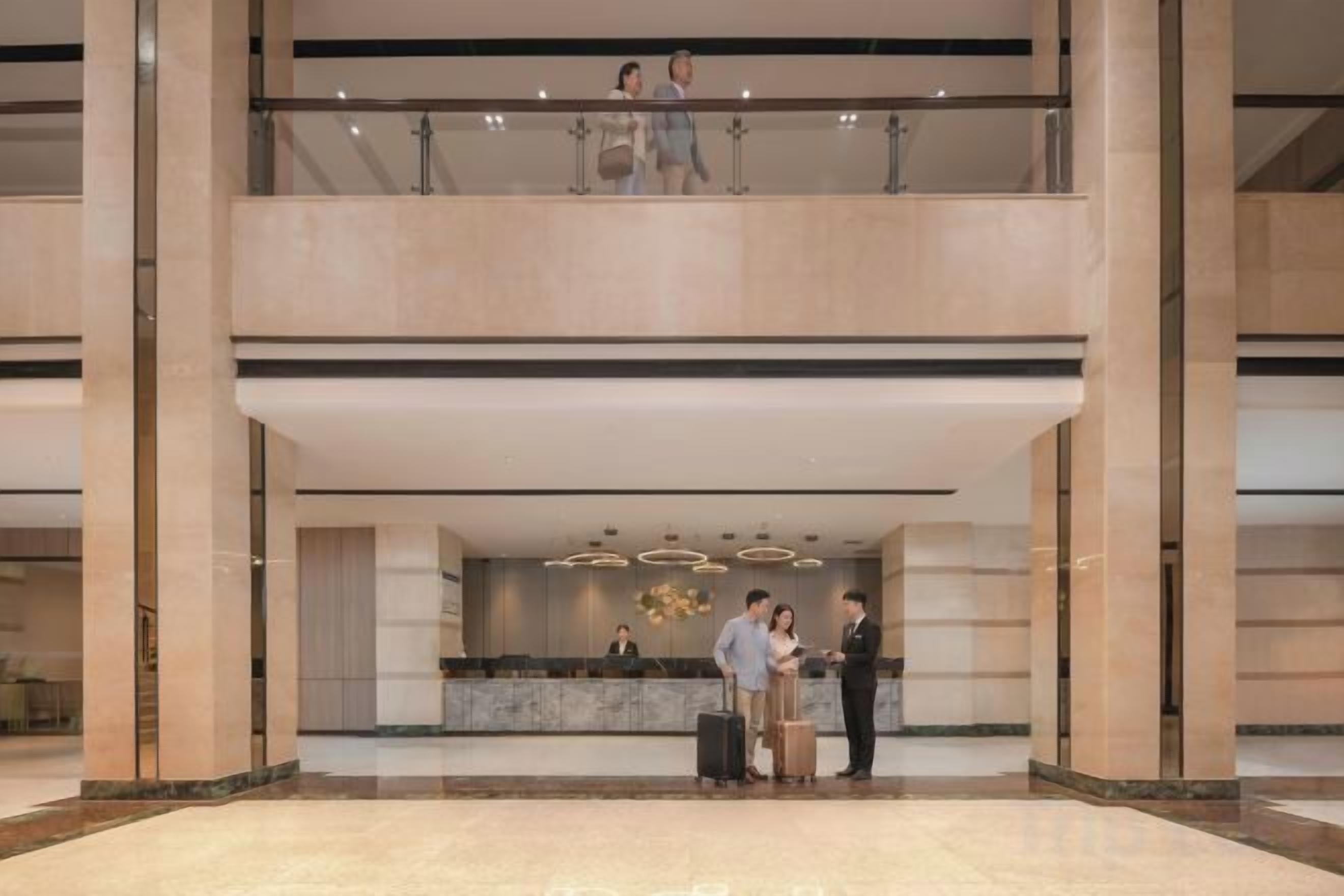 Un hall de hotel con mostrador de recepción, un balcón bajo y un área amplia con piso de mármol.