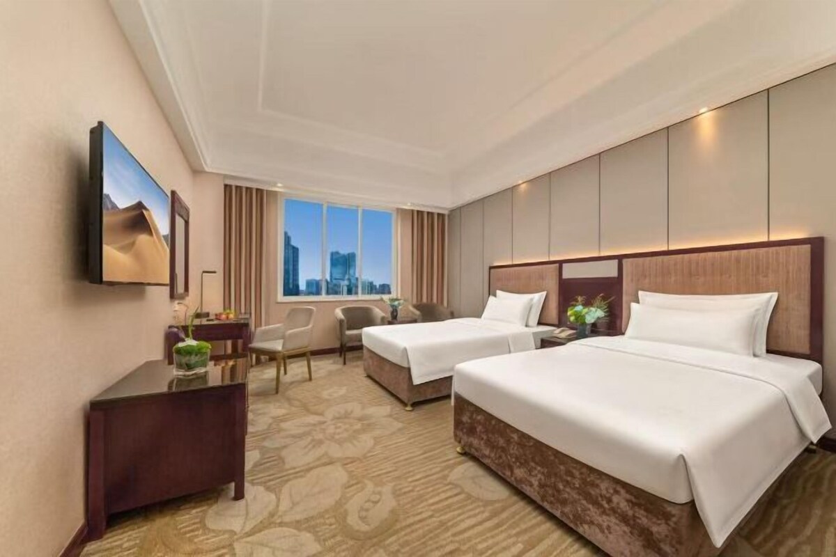 A hotel room with two beds, a desk, a chair, and a TV.