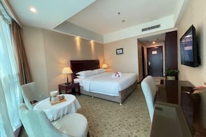 A hotel room with a bed, bedside lamps, a desk, a chair, a small table with a tray, and a television on the wall. - ChangSha Sanhe Hotel (Changsha)