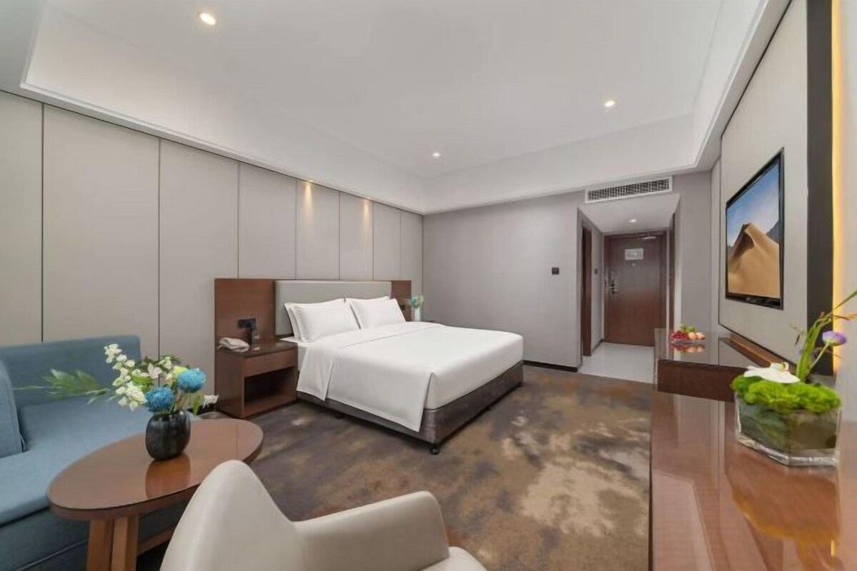 A hotel room with a bed, a sofa, a desk, and a small table with a vase of flowers.