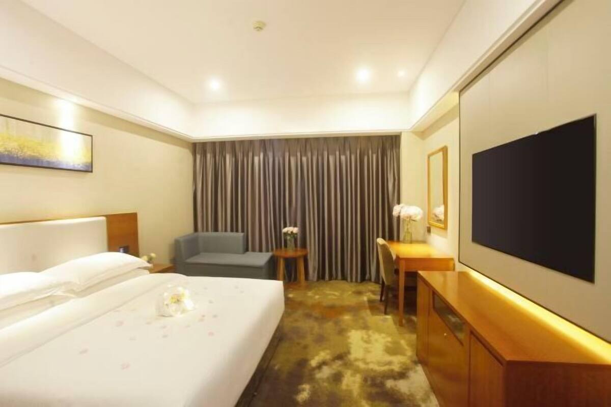 A hotel room with a bed, a desk, a chair, a television, and a curtain.