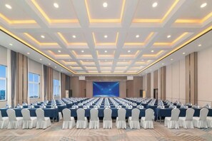 A conference room with rows of tables and chairs, a large screen at the front, and a cityscape view through the windows. - ChangSha Sanhe Hotel (Changsha)