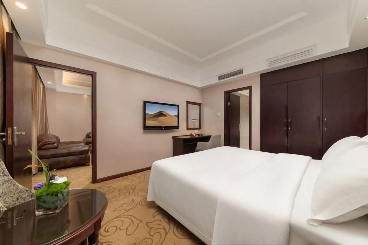 A hotel room with a bed, a desk, a chair, a TV, and a wardrobe.