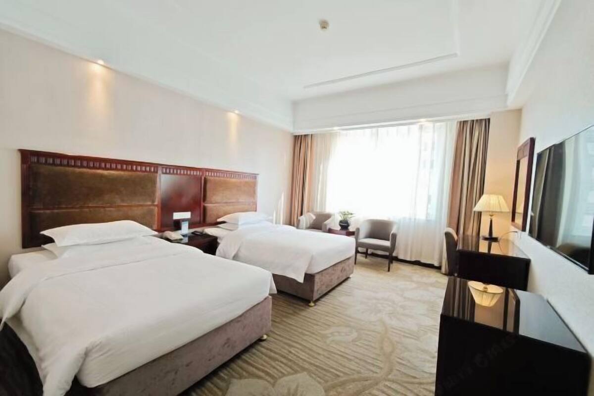 A hotel room with two beds, a desk, a chair, a TV, and a window with curtains.