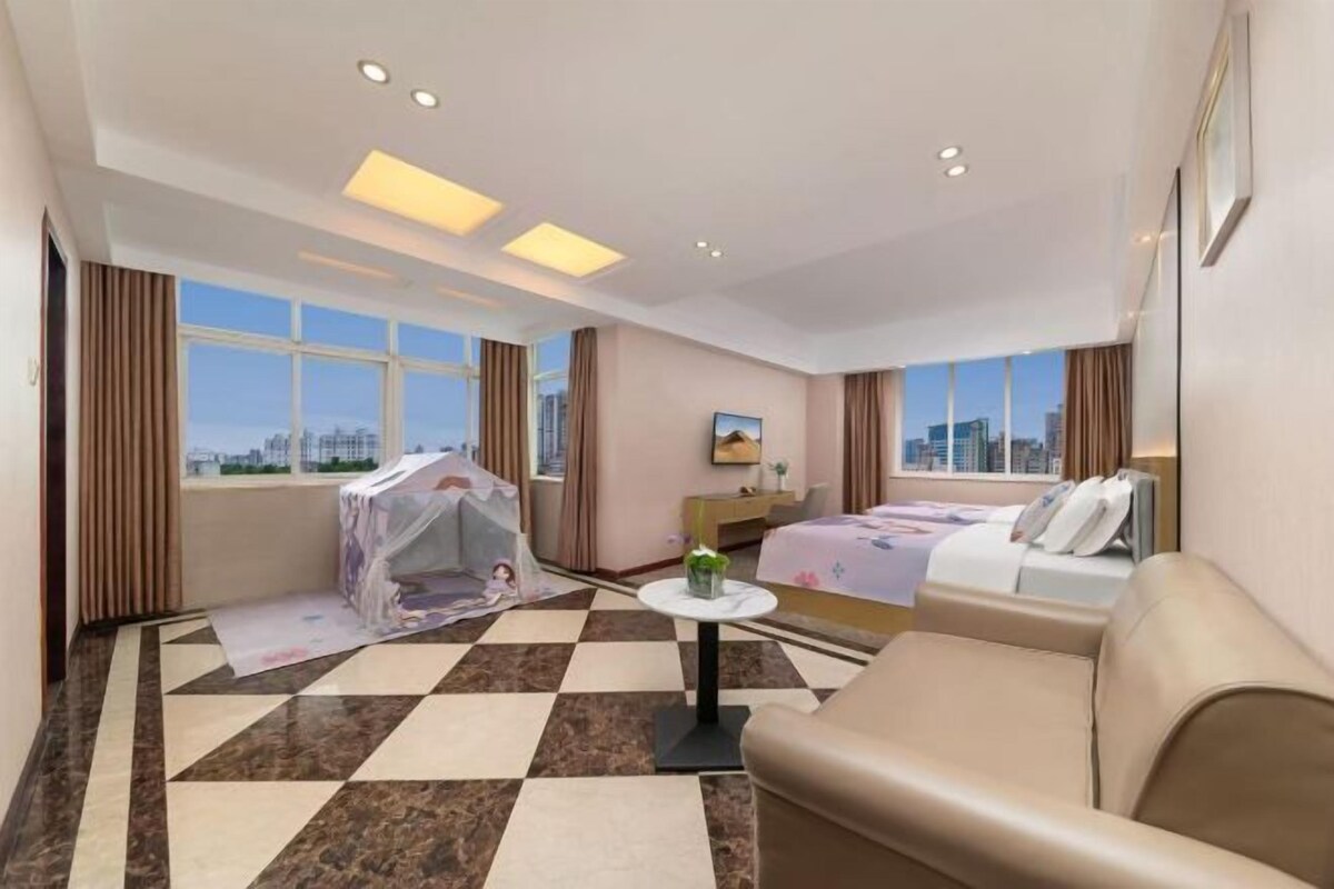 A hotel room with a bed, a sofa, a small table, and a window with a city view.