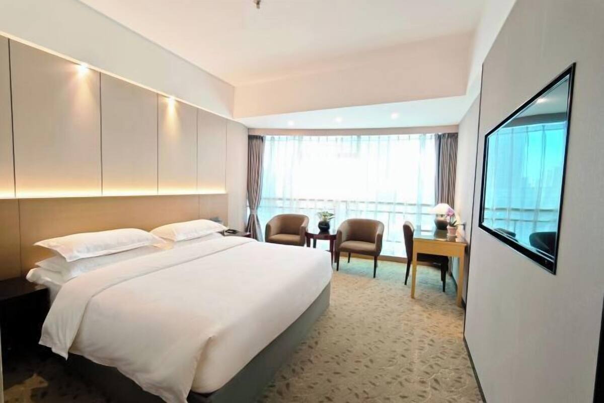 A hotel room with a bed, a desk, two chairs, and a large window.