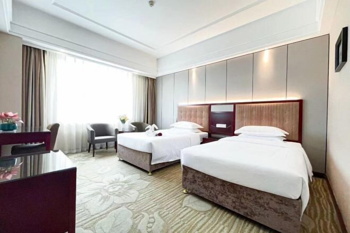 A hotel room with two beds, a desk, and a chair.