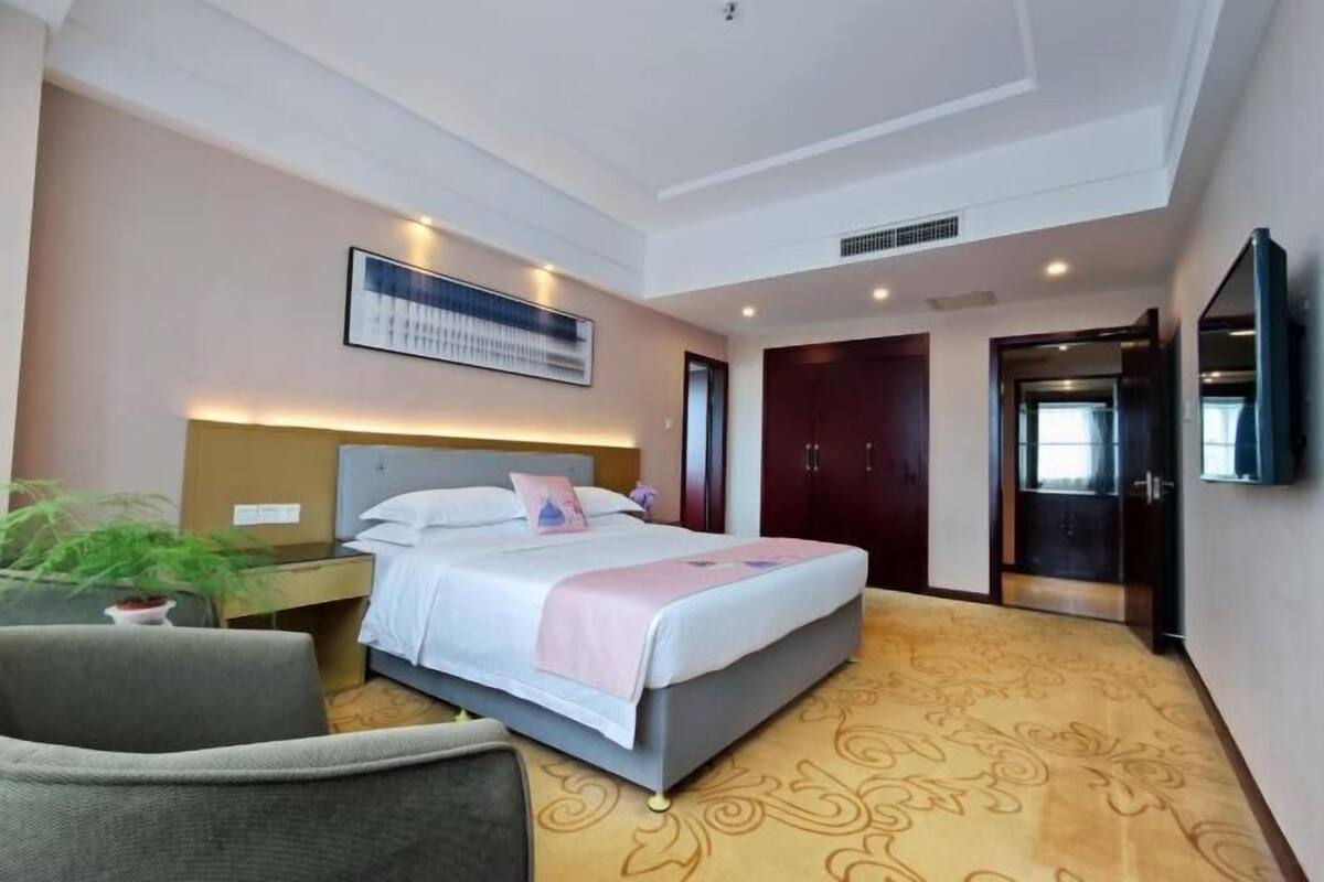 A hotel room with a bed, bedside table, chair, and a large mirror.