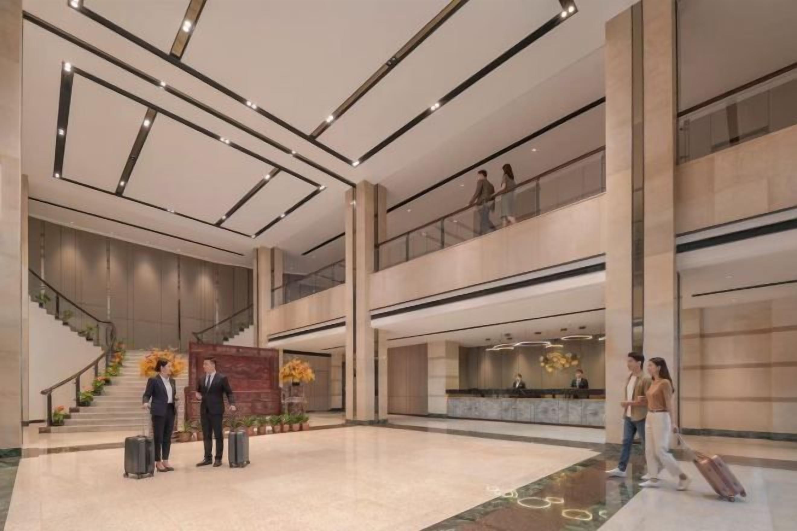 A spacious lobby with a staircase, a reception desk, and a high ceiling with linear lighting.