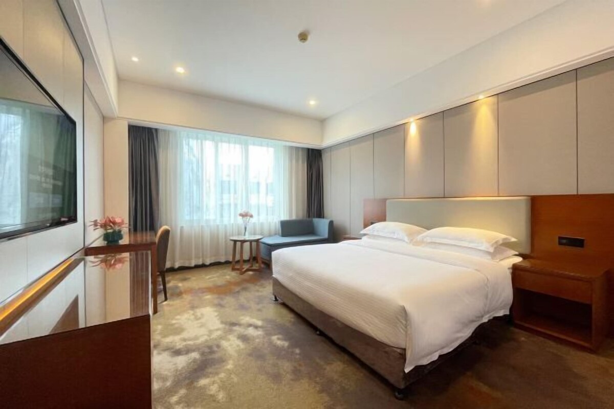 A hotel room with a large bed, a desk, a chair, a small table, and a window with curtains.