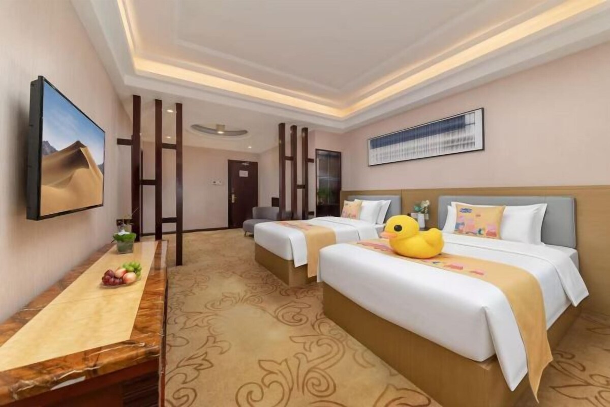 A hotel room with two beds, a desk, and a TV.