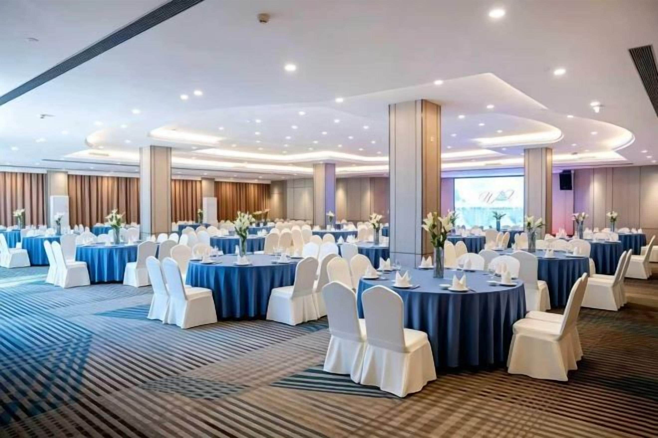 Un salón de banquetes con mesas redondas, sillas blancas y manteles azules.