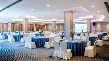Un salón de banquetes con mesas redondas, sillas blancas y manteles azules.