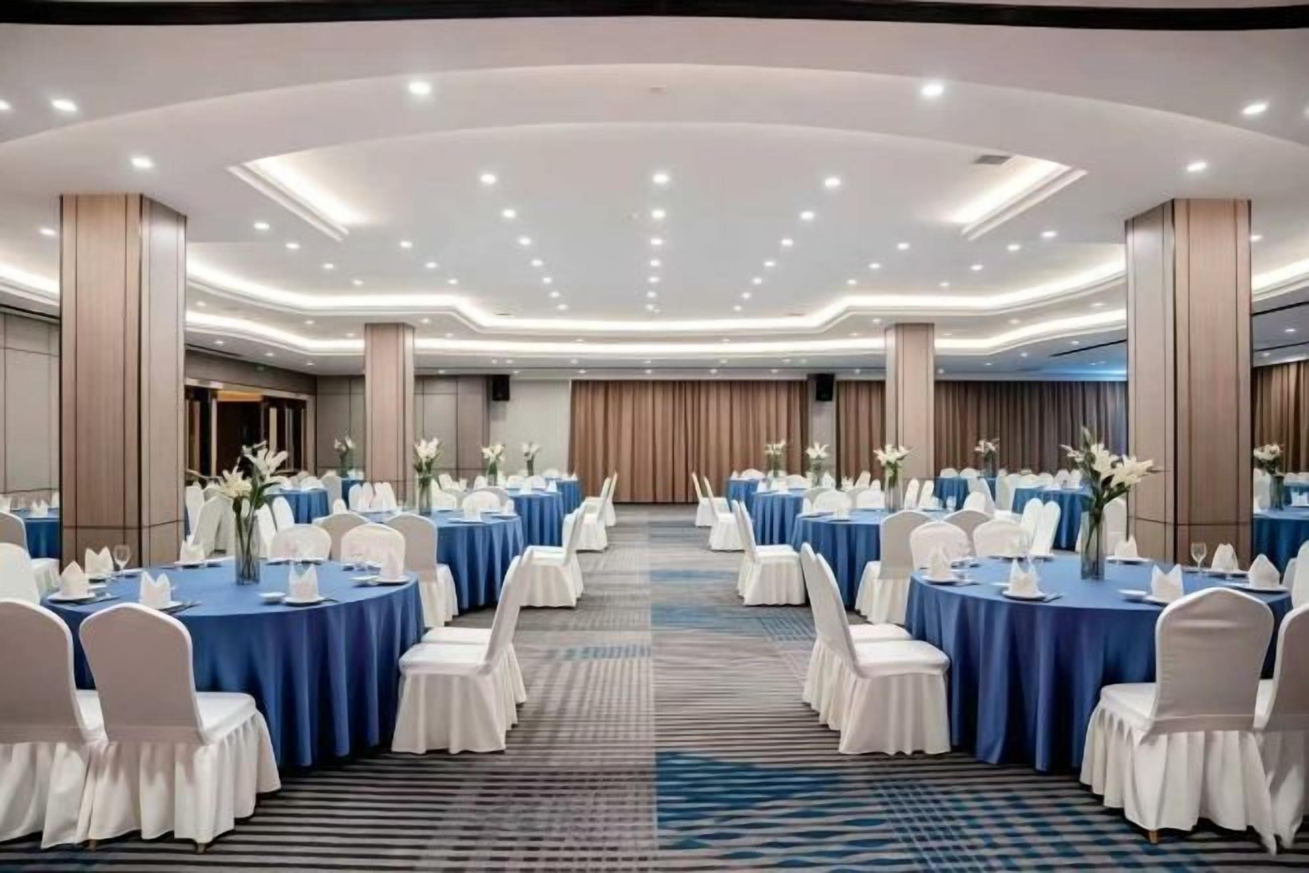 Un salón de conferencias con mesas redondas, sillas blancas y manteles azules.