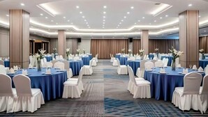 Una sala conferenze con tavoli rotondi, sedie bianche e tovaglie blu.