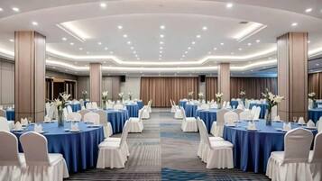 Un salón de conferencias con mesas redondas, sillas blancas y manteles azules.