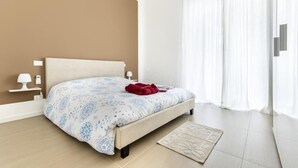 Un dormitorio con cama, mesitas de noche, lámpara y ventana con cortinas.