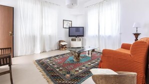Una sala de estar con una mesa de centro de vidrio, un sofá, un televisor y una alfombra estampada.