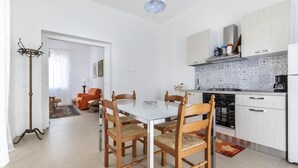 Una cocina moderna con armarios blancos, salpicadero de azulejos y un comedor con mesa blanca y sillas de madera.