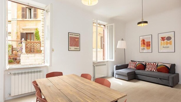 Ein modernes Wohnzimmer mit einem Holzesstisch, einem grauen Sofa und Blick auf ein Gebäude.