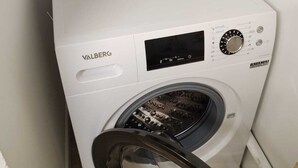 A compact white Valberg washing machine in a small laundry room with a wooden shelf above and a black chair in front. - Provencal house for 14 sleeps with private garden. Perfect for family gatherings (La Crau)
