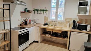 A compact kitchen with a stove, oven, sink, and microwave. There is a window with a view of the outside, and a shelf with kitchen utensils. - Provencal house for 14 sleeps with private garden. Perfect for family gatherings (La Crau)