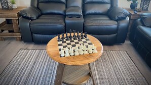 A living room with a black leather sofa, a wooden coffee table with a chessboard, and a striped rug. - The Man Cave. Perfect for traveling workers and a great place for families  (Greybull)