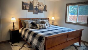 A bedroom with a wooden bed, two bedside tables with lamps, a large window, and wall art. - The Man Cave. Perfect for traveling workers and a great place for families  (Greybull)