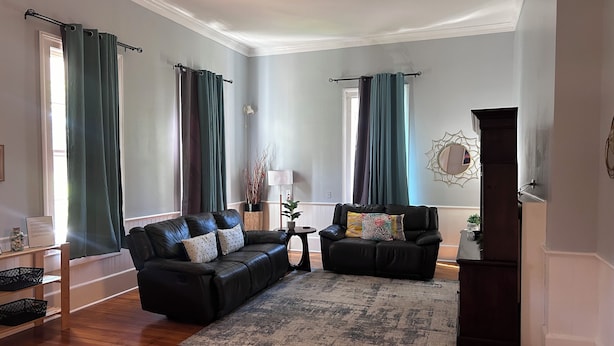 A living room with two black leather sofas, a patterned rug, and a dark wooden cabinet.