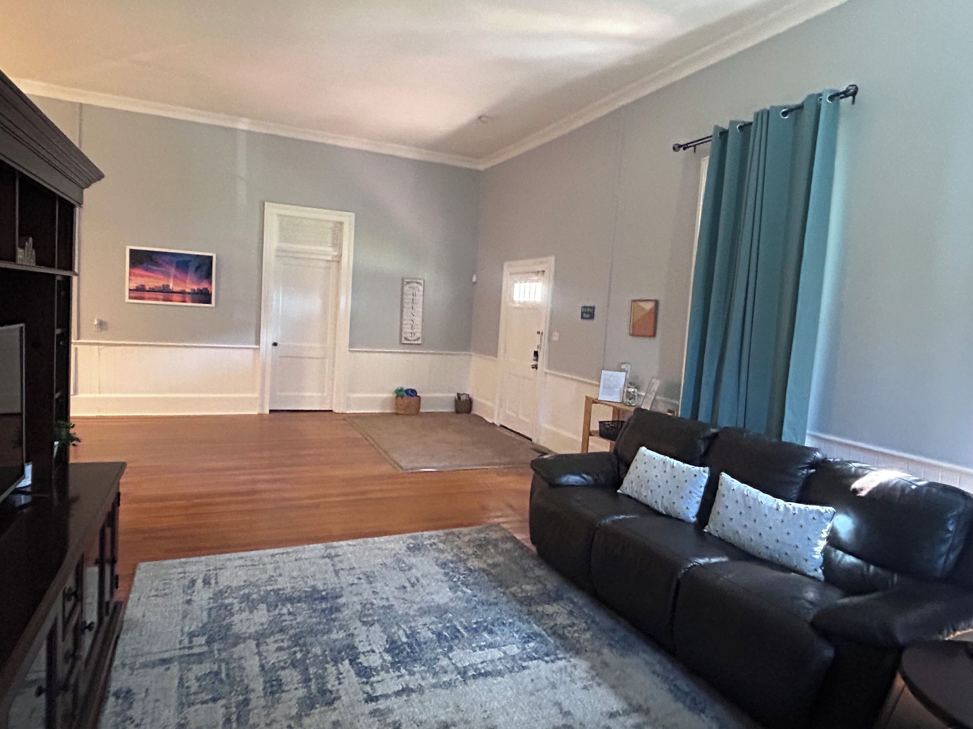 A living room with a dark leather sofa, a patterned rug, and a wooden floor.