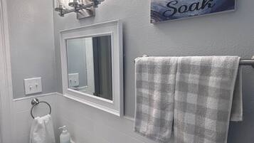 Un baño con un lavamanos blanco, un espejo, un perchero con dos toallas, un dispensador de jabón y un letrero que dice 'Soak'.