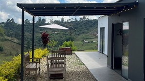 Een overdekt terras met een pergola, houten stoelen en een tafel, met uitzicht op een bergachtig landschap.