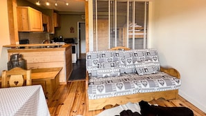 A compact living space with a kitchenette, a sofa with patterned cushions, and a wooden bench. - Comfortable studio with pool and view (Saint-Gervais-les-Bains)