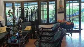 A spacious living room with wicker furniture, a glass coffee table, and a view of a garden through large windows. - Casa de Campo (El Valle de Antón)