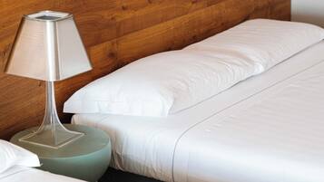 Un lit avec du linge de lit blanc, une tête de lit en bois et une lampe sur une table de chevet ronde.
