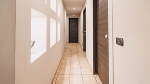 A hallway with a tiled floor, a door with a number, and a light switch on the wall. - Locanda Da I Baldi (Laveno Mombello)