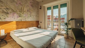 A hotel room with a large bed, a wooden headboard, a potted plant, a chair, and a view of the outside through a sliding door. - Locanda Da I Baldi (Laveno Mombello)