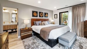 Ein modernes Schlafzimmer mit einem großen Bett, Nachttischen, einer Bank, einem Spiegel und Kunstwerken an der Wand.
