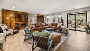 Ein geräumiges Wohnzimmer mit einem großen, winkelförmigen Sofasessel, einem runden Couchtisch und verschiedenen Sitzgelegenheiten, darunter ein Sessel und ein Hocker.